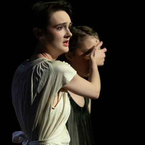 A woman in a nightgown wears a concerned expression as she covers the eyes of a younger woman next to her in a black nightgown in front of a deep black background. They are singing. Image credit Richard M. O'Dell. Actors: Maeve Z. O'Connor, Aaliyah Foote